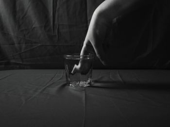Close-up of woman hand in glass of water against black background