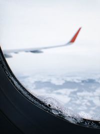 Airplane flying over frozen lake against sky