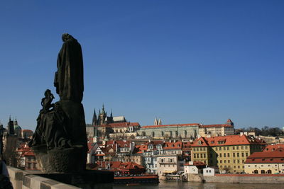 Statue by buildings against clear blue sky