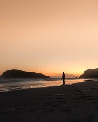 Silhouette person standing on beach against clear sky during sunset