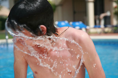 Close-up of boy shaking wet hair by swimming pool