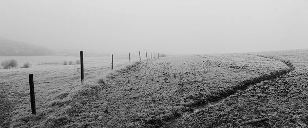 Wooden fence on snow covered land against sky