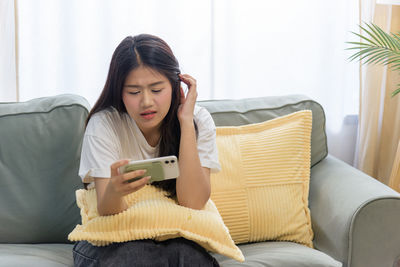 Young woman using phone while sitting on sofa at home