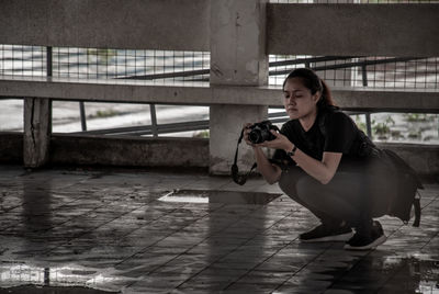 Young woman photographing with camera while crouching outdoors
