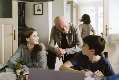 Senior man talking with grandchildren sitting on chair and studying at home