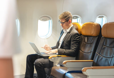 During a flight, a businessman in formal attire and glasses looks out the plane window 