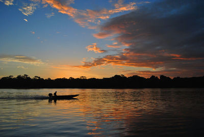 Silhouette person riding boat in lake against sky during sunset