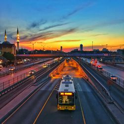 Vehicles on road against sky during sunset in city