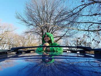 Boy peeking from sun roof against bare trees