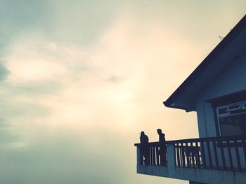 Low angle view of silhouette bird perching on roof against sky