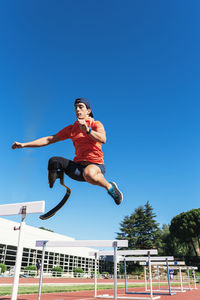 Low angle view of man jumping against clear blue sky