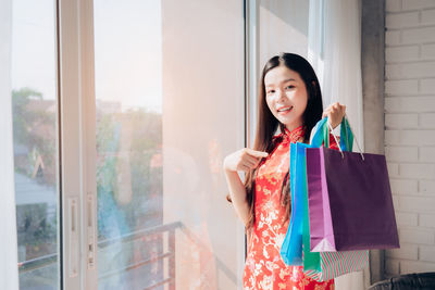 Portrait of a smiling young woman standing against window