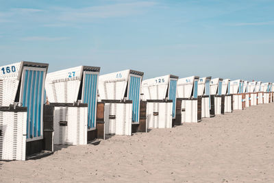 Hooded beach chairs on sand against sky