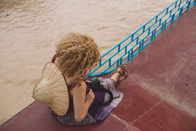 High angle view of mid adult woman with hat sitting over lake on wall