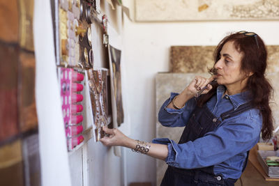 Female artist looking paintings on wall in workshop