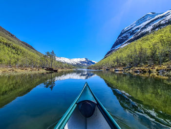 Scenic view of canoe on lake and mountains against blue sky