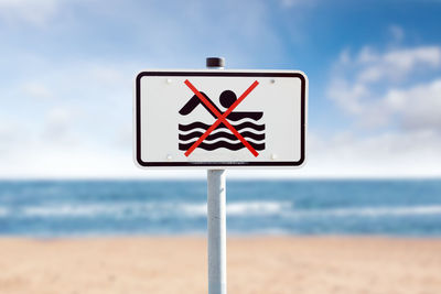 Close-up of road sign by sea against sky