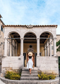 Young woman in white dress standing on stairs of an old building, town, street.