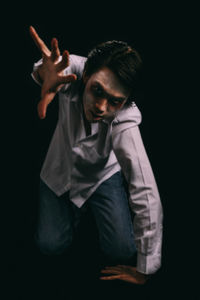 Portrait of young man with halloween make-up kneeling against black background