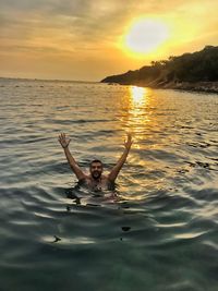 Man swimming in sea against sunset sky