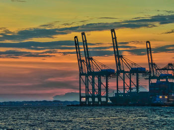 Silhouette cranes against orange sky during sunset