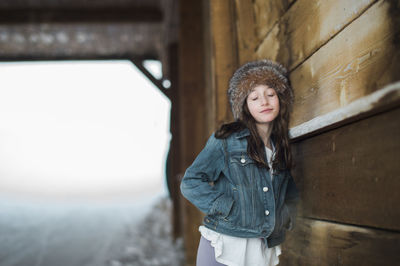 Girl in fur headband leaning against a bridge with eyes closed