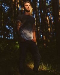 Man with hands in pockets standing against trees on field