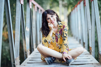 Portrait of smiling woman sitting on footbridge