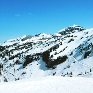 Low angle view of snowcapped mountains against clear blue sky