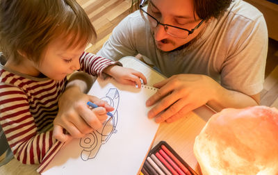 High angle view of father assisting son in drawing