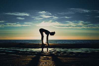 Silhouette woman standing on beach against sky during sunset