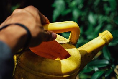 Cropped hand of man holding yellow watering can