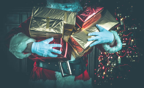 Midsection of man wearing santa claus costume holding christmas presents at home