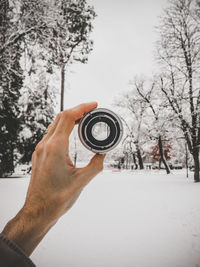 Cropped hand of person holding lens against bare tree during winter