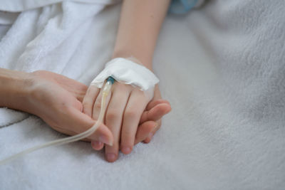 Close-up of mother holding hands of medicated child on bed at hospital