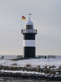 Lighthouse by sea against sky during winter