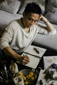 Man writing in book while sitting with herbs and candles at table