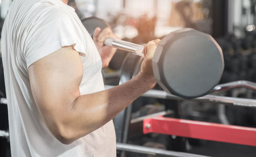 Midsection of man lifting dumbbell in gym