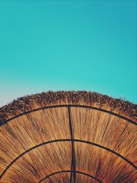 Directly below shot of thatched roof parasol against clear blue sky