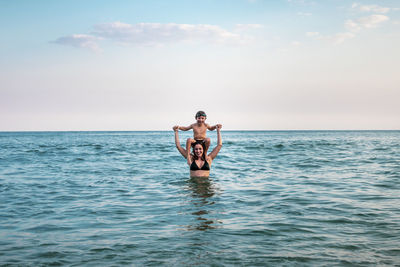 5 years old kid on top of his mother's shoulders, into the ocean