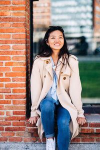 Portrait of beautiful young woman standing against brick wall