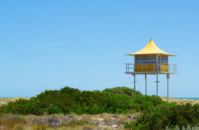 Lifeguard tower amidst trees and building against clear blue sky