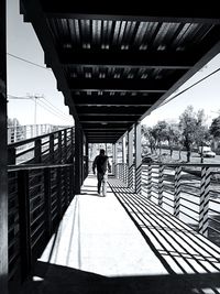 Man walking on footbridge against sky