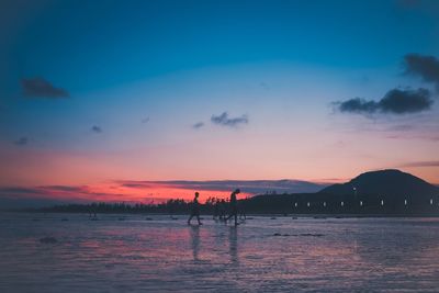 Silhouette people on beach against sky during sunset