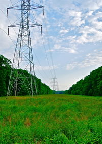 Electricity pylon on grassy field against cloudy sky