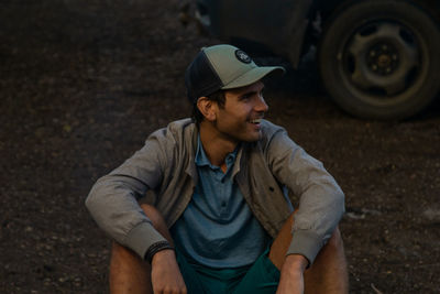 Smiling young man looking away while sitting against car