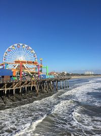 Ferris wheel on beach against clear blue sky