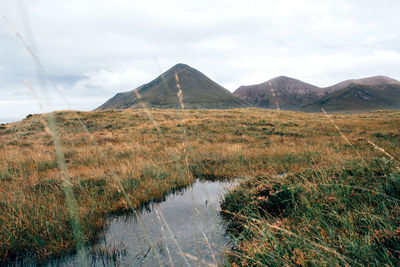 Narrow stream along landscape and mountains against sky