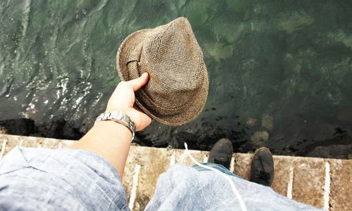 Low section of a man holding hat against water