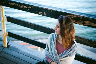 Thoughtful young woman sitting on pier over sea